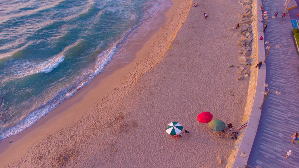 Aerial view of a sandy beach with colorful umbrellas at twilight, perfect for summer leisure.