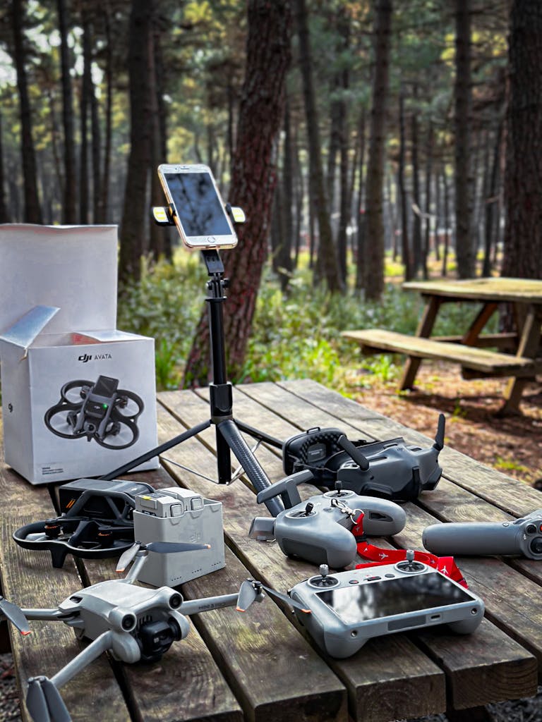 Various drone accessories arranged on a picnic table in a forest, showcasing technology outdoors.
